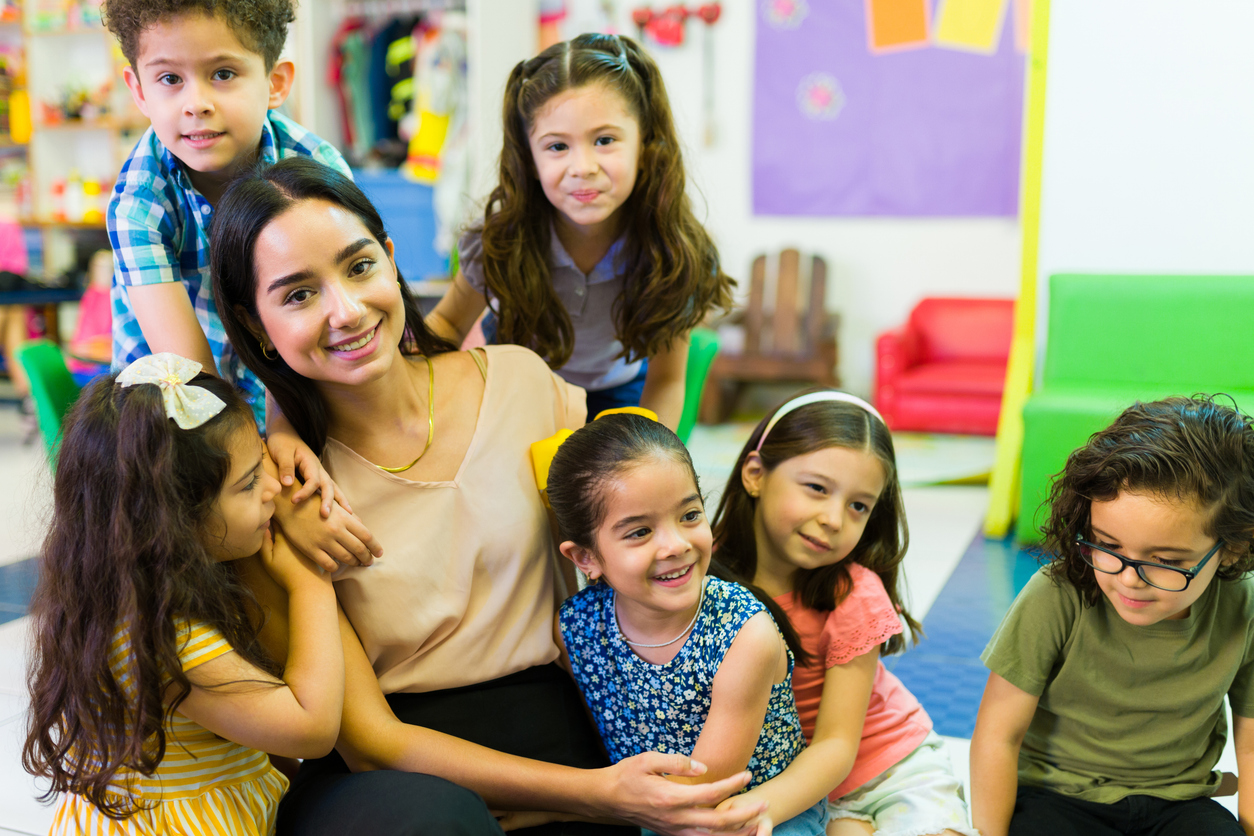 Latin teacher smiling while hugging and playing with her preschool children students in the classroom