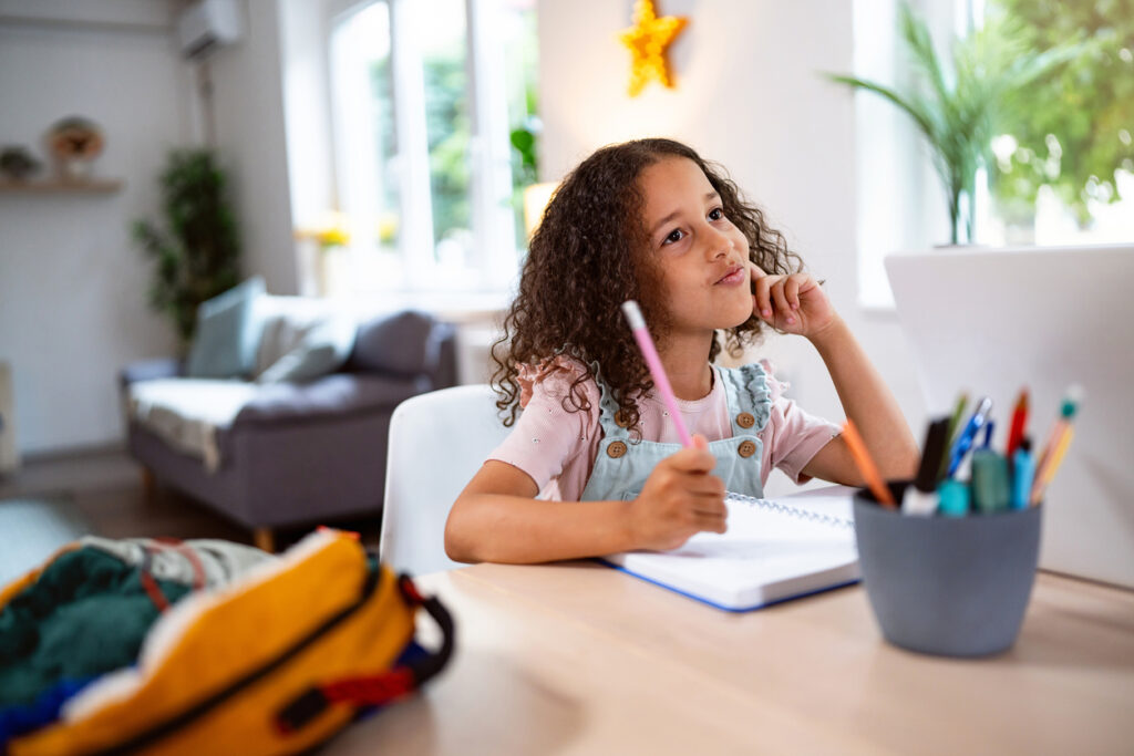 Adorable multiracial girl doing her homework, at home for the dining table