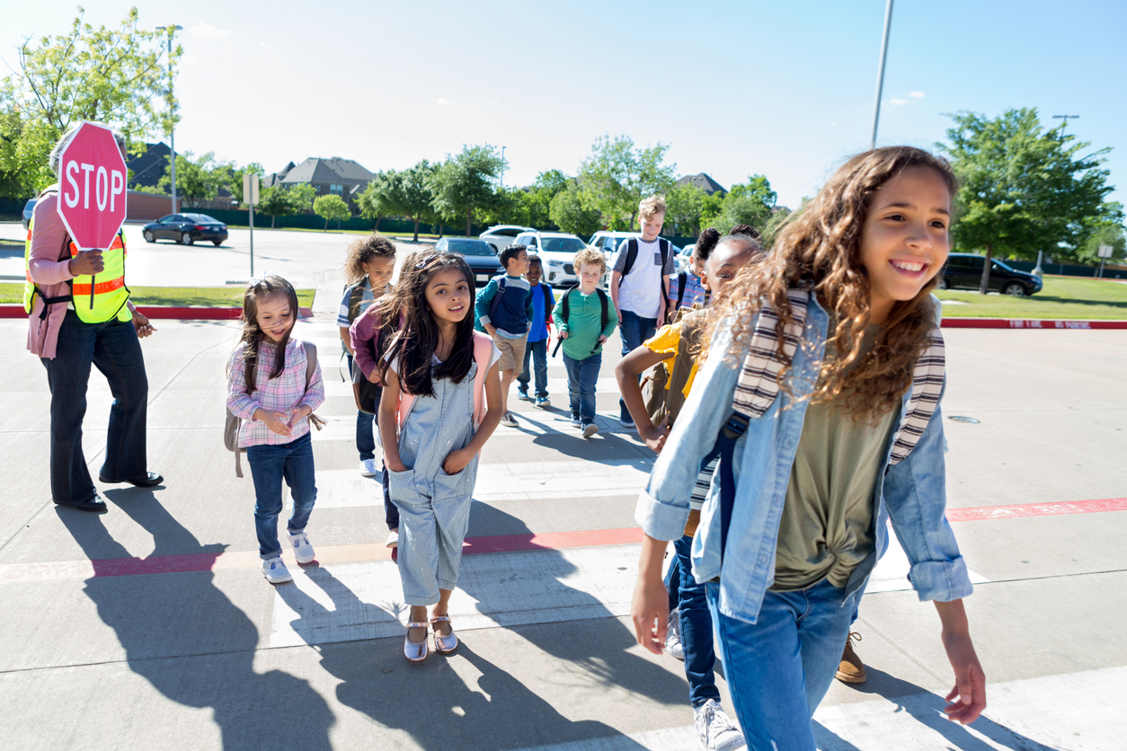 Smiling mixed race preteen girl walks across a crosswalk. Other students are walking in the background.