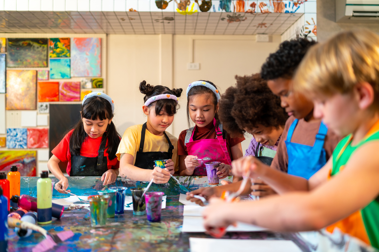 Group of Diversity school children learning acrylic pouring art on canvas workshop with teacher at art studio. Happy boys and girls enjoy and fun with colorful abstract modern art painting in classroom.